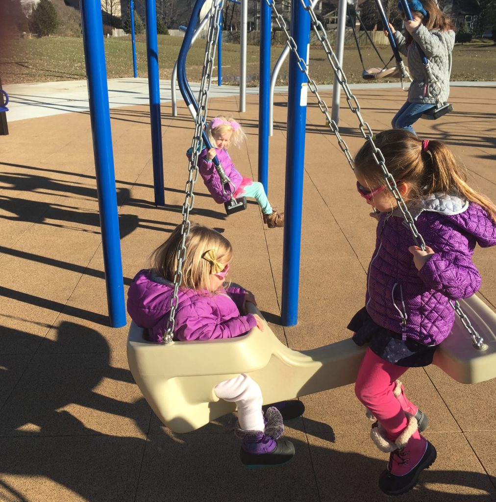 4 girls swinging on face to face swings in Sunpoint Park.