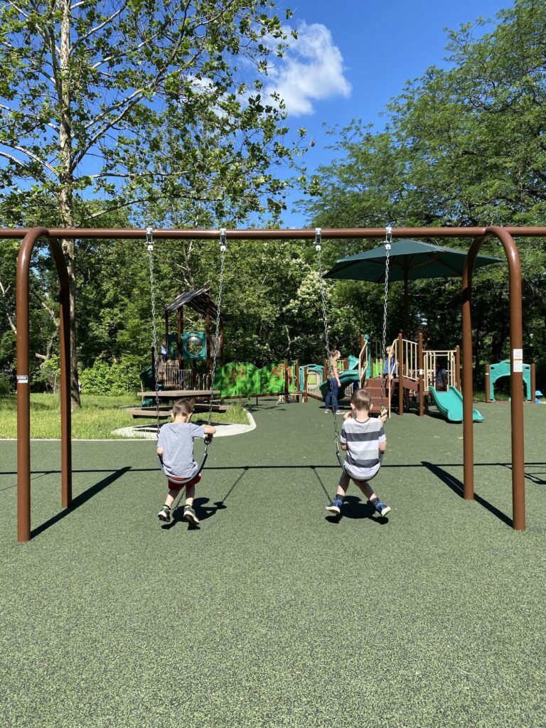 Two boys on a swingset at the park.