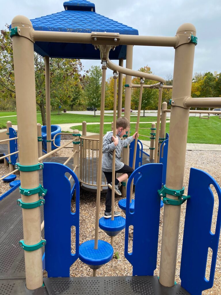 A boy climbing through bars on the playground.