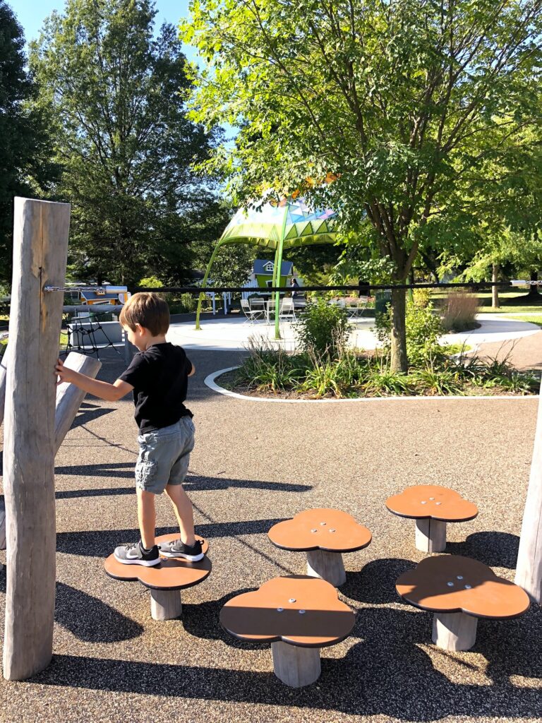 A boy walking on flower shaped pads in the park.