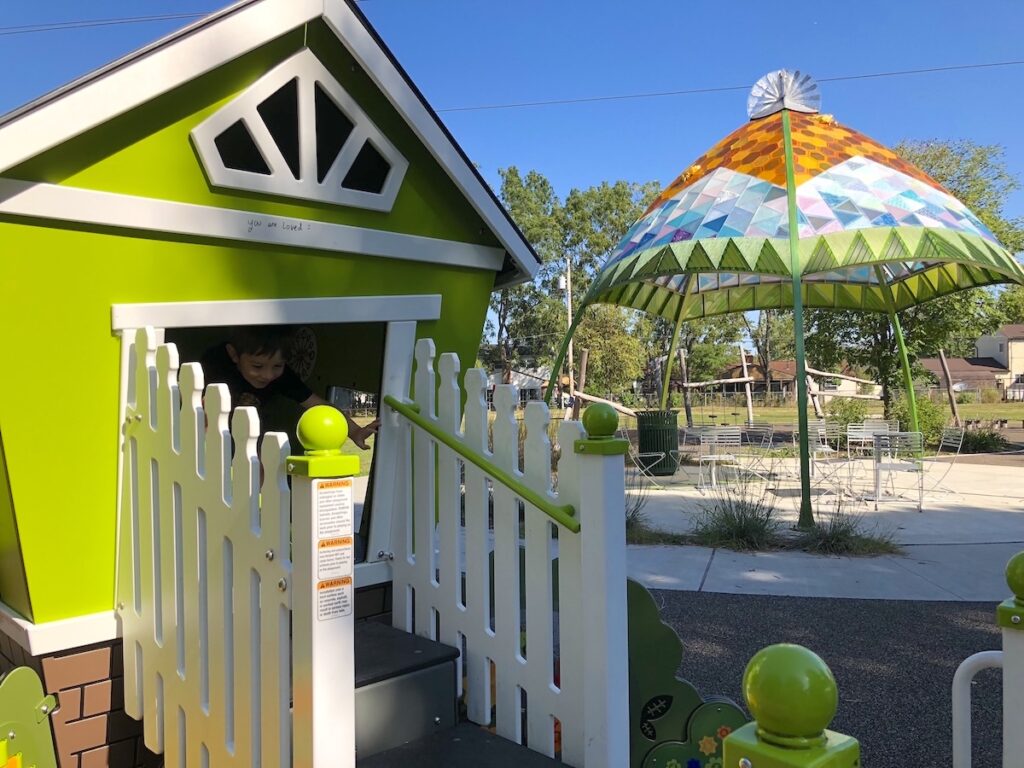 A green playhouse and a stained glass pavilion in the park.