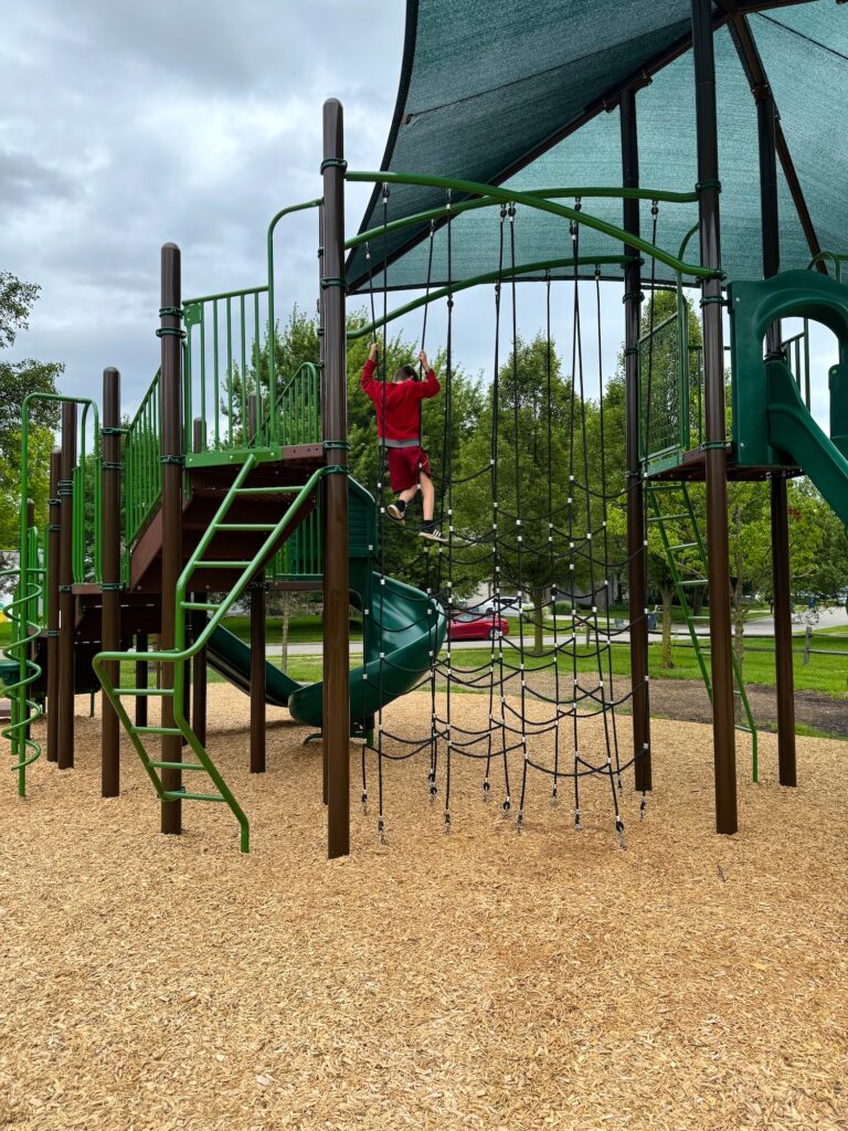 A boy climbing across the ropes at Ambassador Commons Park.