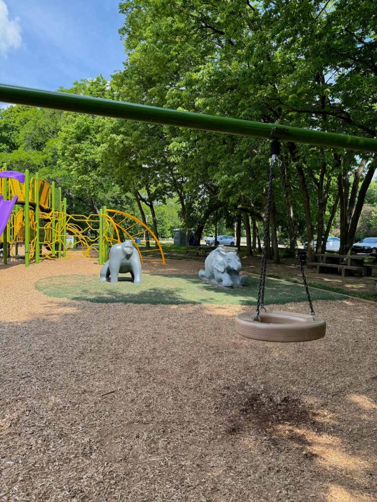 A tire swing in front of a play gorilla and elephant on the playground at Whetstone Park.